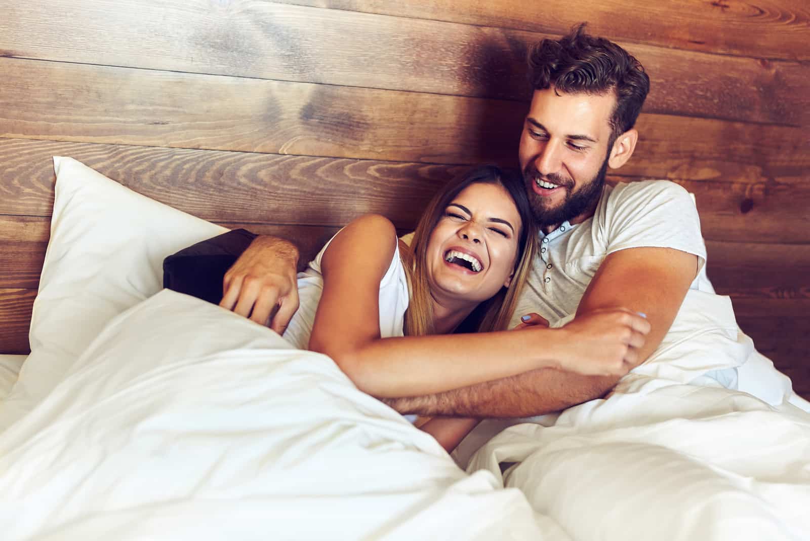 Junges Paar liegt im Bett und lacht beim Kitzeln