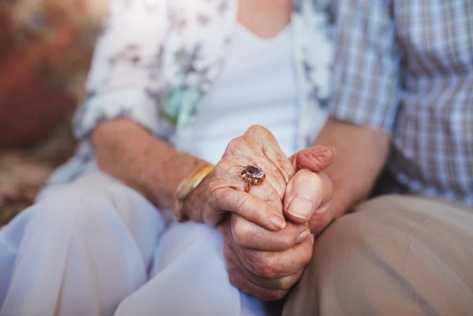 Älteres Ehepaar, das Händchen hält, während es zu Hause zusammensitzt