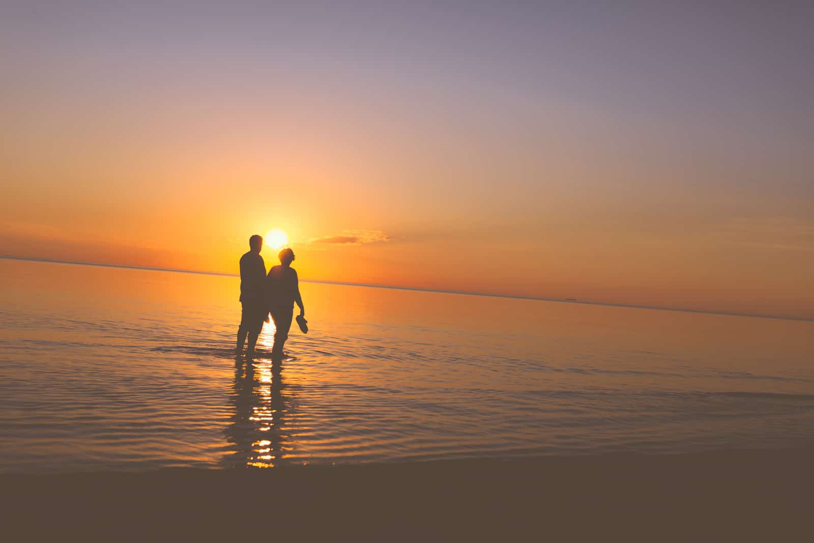 Älteres Paar, das bei Sonnenuntergang am Ufer entlang geht