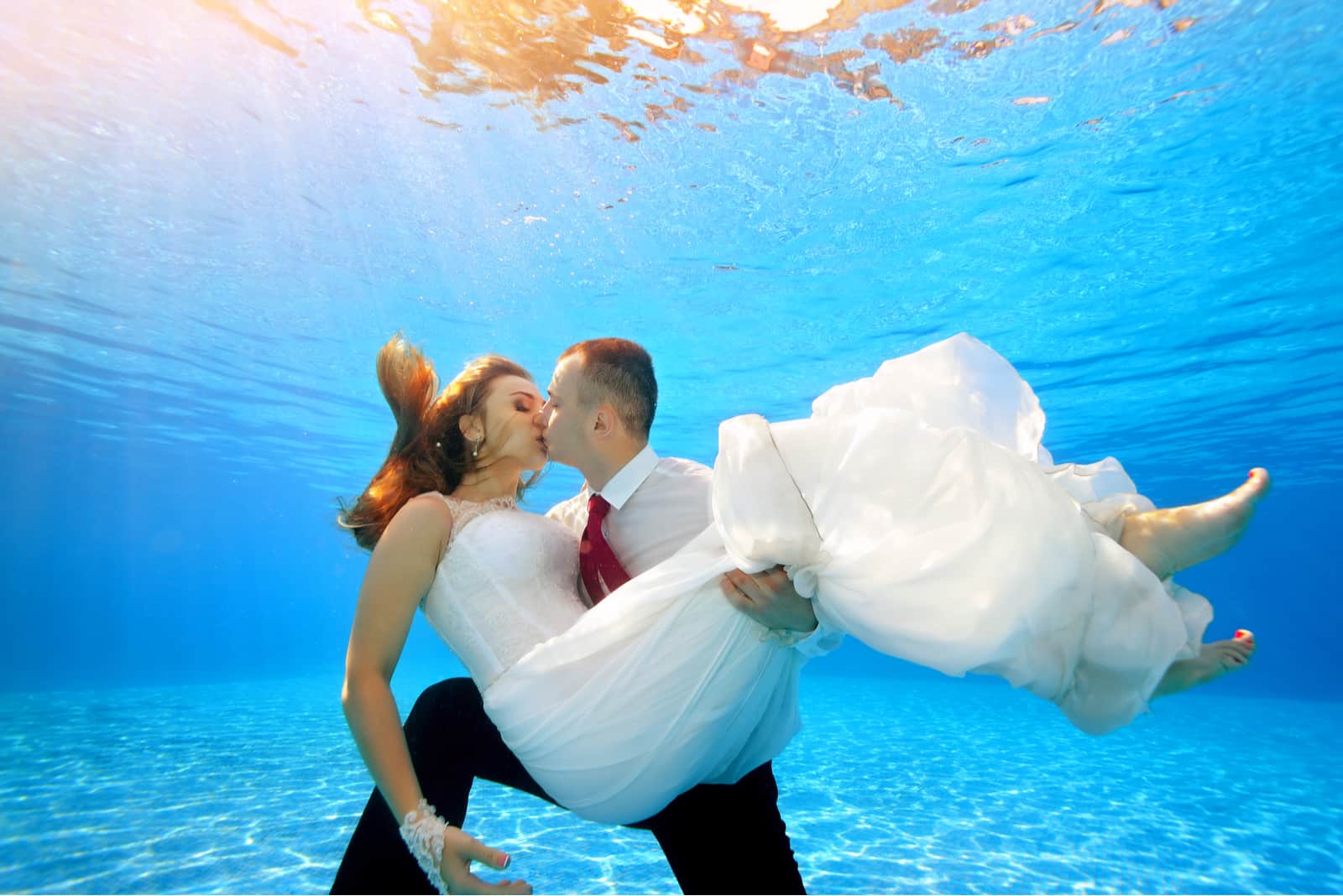 Der glückliche Bräutigam hält die Braut unter Wasser in den Armen
