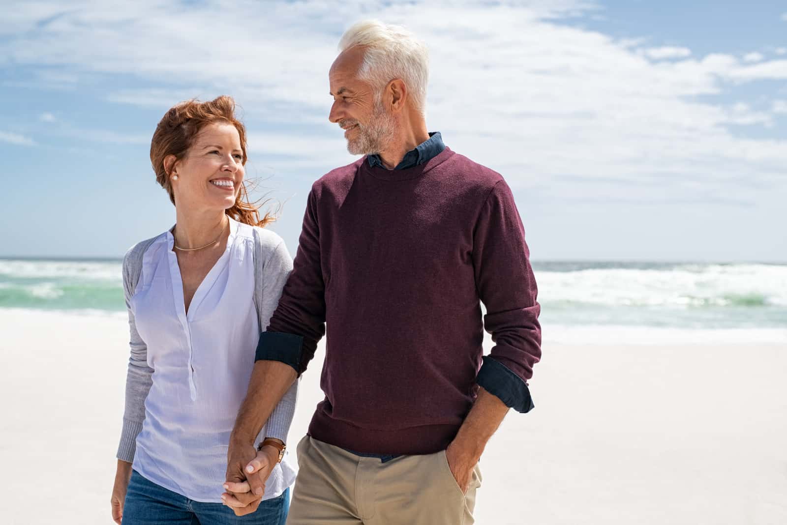 Glückliches älteres Paar, das an einem sonnigen Tag am Strand spazieren geht