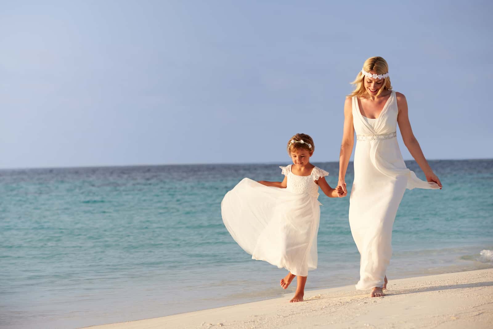 Braut mit kleinem Mädchen, das am Strand spazieren geht