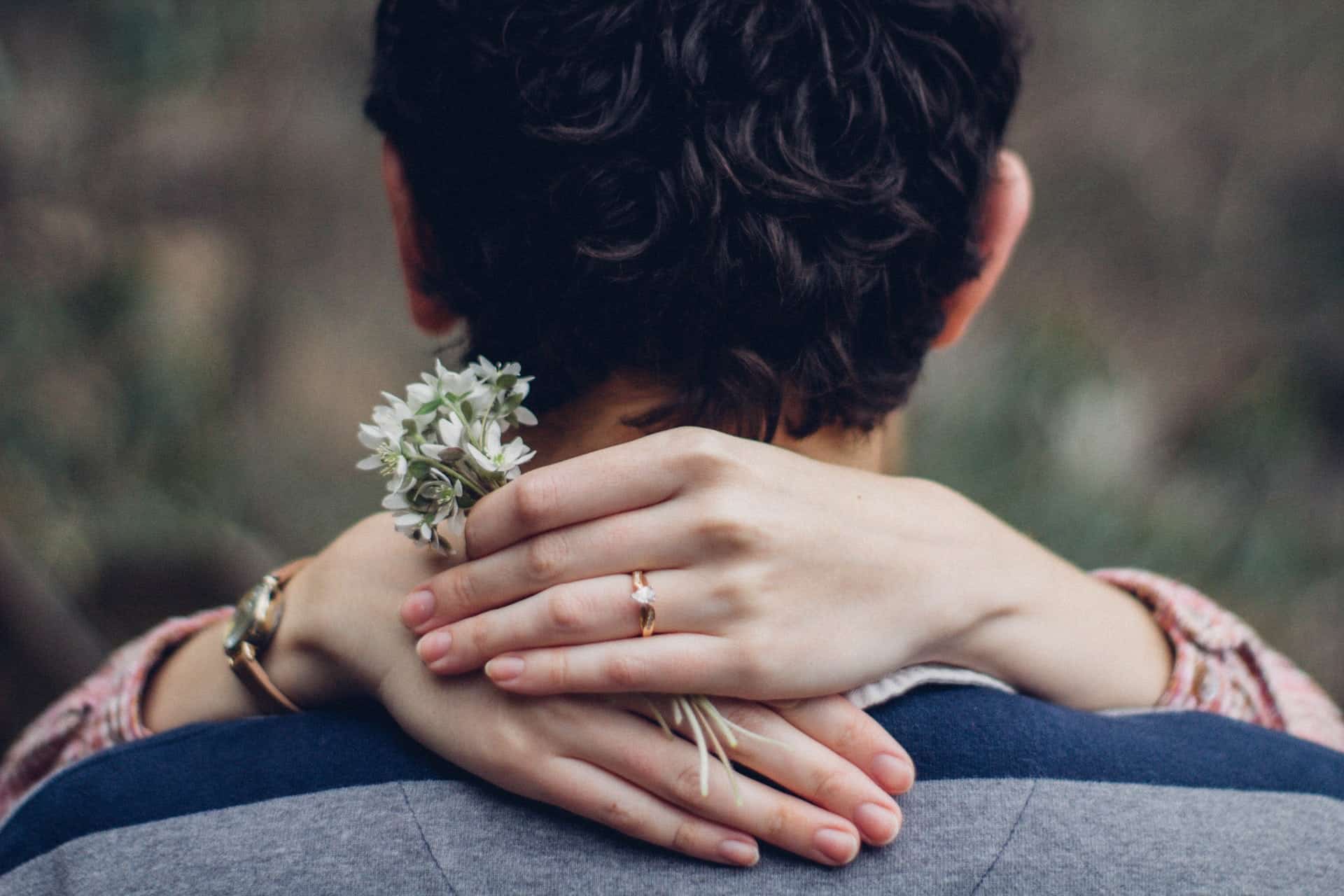 Frau umarmt ihren Mann um den Hals und hält Blumen