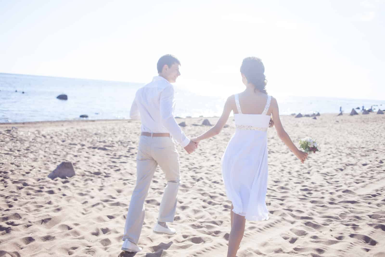Frisch verheiratetes glückliches Paar, das an einem Sandstrand läuft