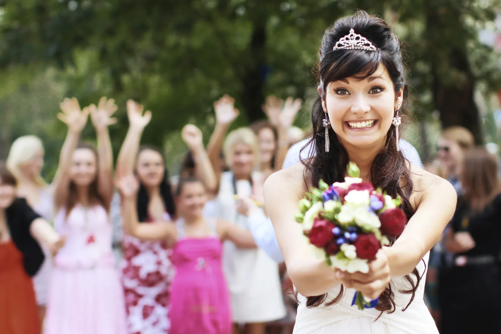 Braut wirft einen Blumenstrauß mit Hochzeitsgästen im Hintergrund