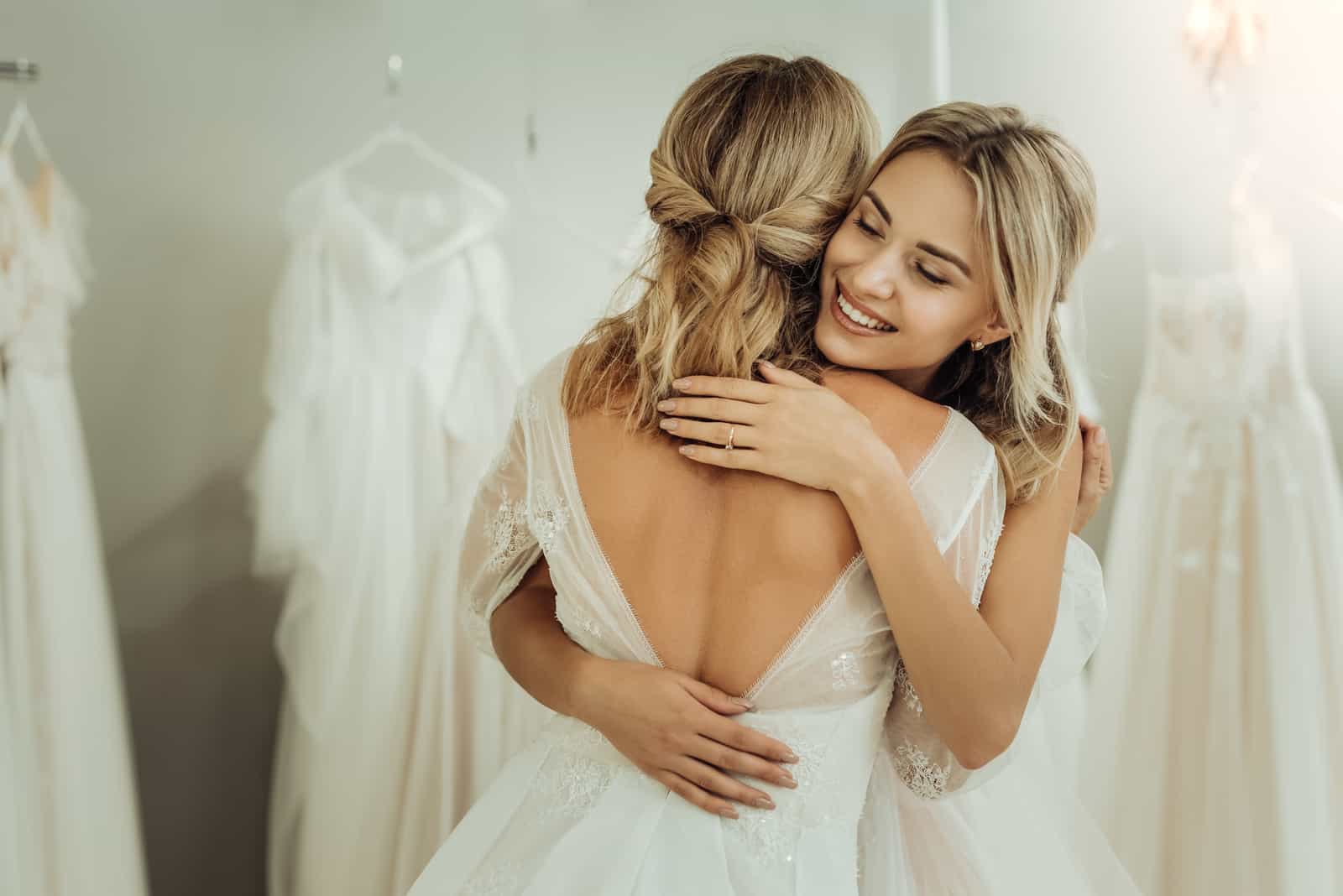 Braut und Trauzeugin umarmen sich im Kleiderladen